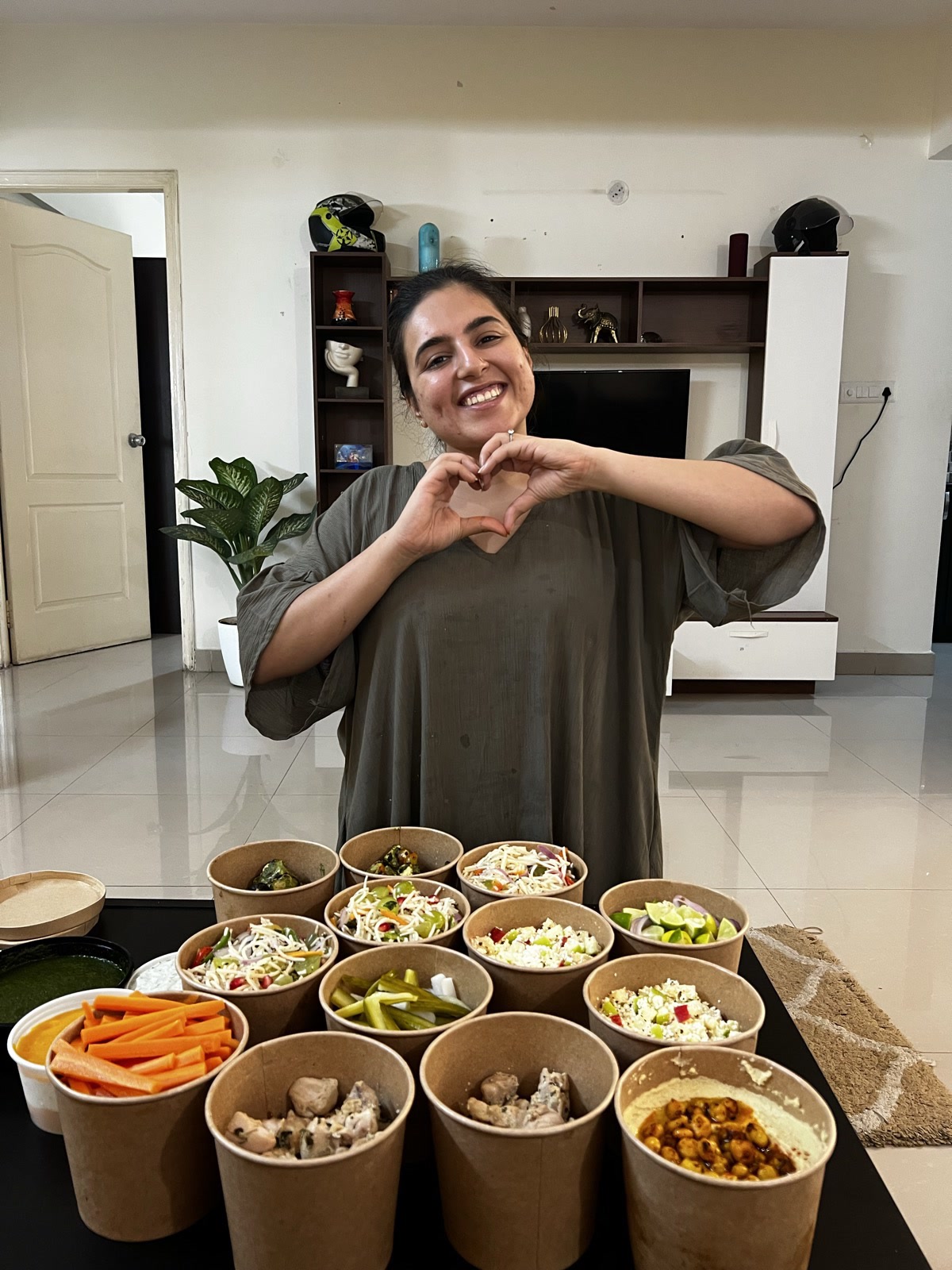 Pooja making a heart with her hands behind a spread of her home-cooked food
